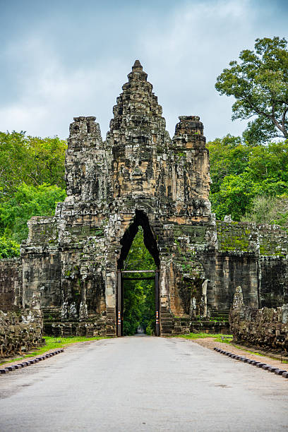 A detailed view of the sculpted stone gateway of Angkor Thom nestled within lush greenery, showcasing the architectural heritage of Cambodia.