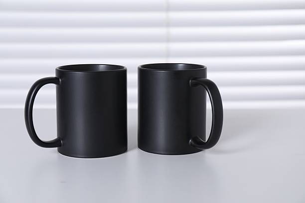 istock Blank black ceramic mugs on white table. Mockup for design 2232362716