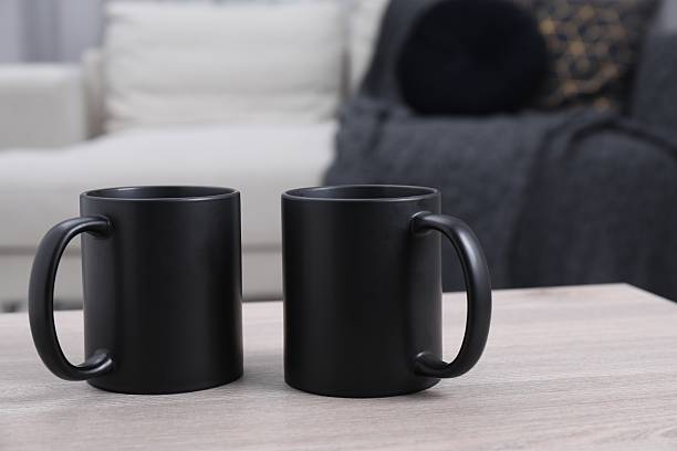 istock Blank black ceramic mugs on white wooden table. Mockup for design 2232362739