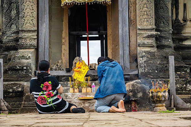 Two individuals are seen kneeling in prayer at an ancient temple site in Angkor, Cambodia, highlighting devotion and cultural richness.