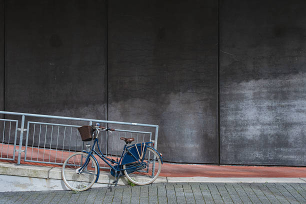 Blue bicycle with basket parked against a dark urban wall outside