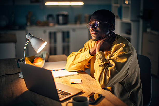 Young black man focused on laptop at home during night-time study session with warm light ambiance