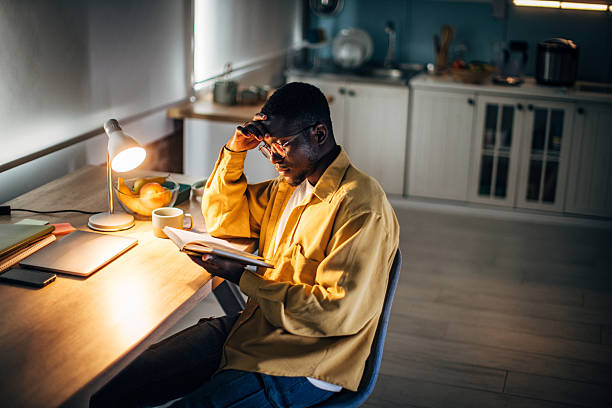 istock Young black man reading at home in the evening in a cozy kitchen setting 2232374049