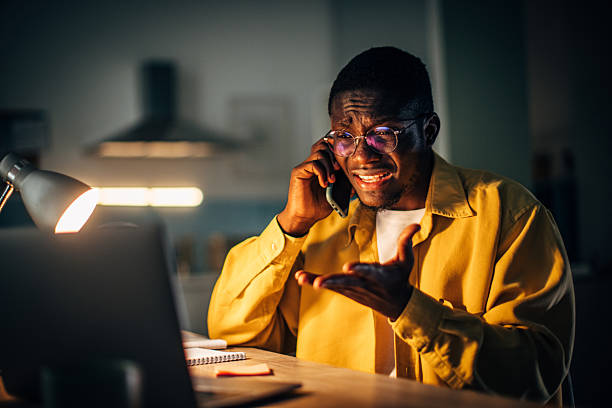 istock Young black man having a late night conversation at home while using a laptop and staying engaged with a phone call 2232375178