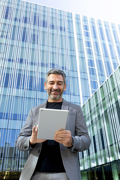 istock Smiling businessman using digital tablet in front of office building 2232375470