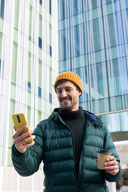 istock Smiling man using smartphone and holding coffee outside office building 2232375510