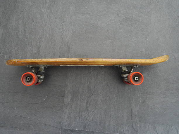 Skateboard is laying on the ground with its wheels off. The skateboard is old and has a wooden deck