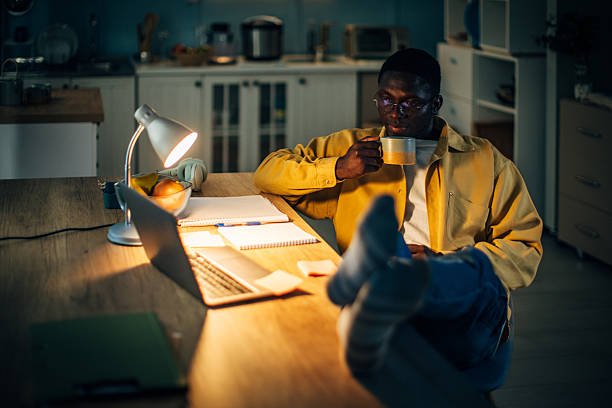 istock Young black man enjoys a warm drink while working at home late at night in cozy kitchen setting 2232376317