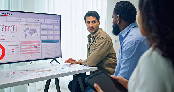 istock Group of business professionals meeting reviewing global data analytics presented on a large screen, discussing strategy and growth at the office. Finance meeting concept. 2232377728