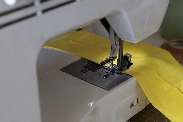A detailed shot captures a sewing machine actively stitching vibrant yellow fabric, highlighting the process of textile creation. The focus is on the needle and presser foot area.