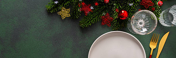 istock A cozy Christmas table with an empty plate and cutlery on a rich green background. Red Christmas tree decorations and spruse branches complete the festive look, banner 2232379647