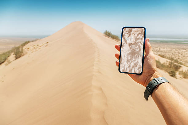 Hand holding a smartphone displaying a GPS navigation map against a stunning desert landscape, highlighting the blend of technology and adventure