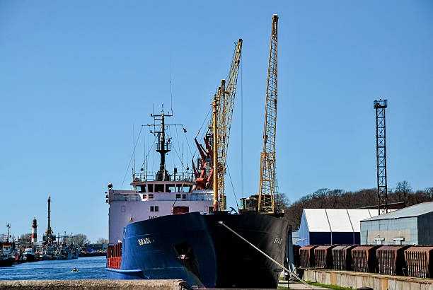 Klaipeda, Lithuania - May 03, 2013 - Large cargo ship docked at industrial harbor with cranes under clear sky.