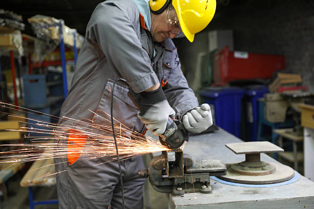 Industrial Worker Wearing Protective Gloves, Safety Glasses, and Helmet Using Angle Grinder to Cut Metal, Creating Bright Sparks in Workshop. Concept of Heavy Industry, Metalwork, and Skilled Labor.