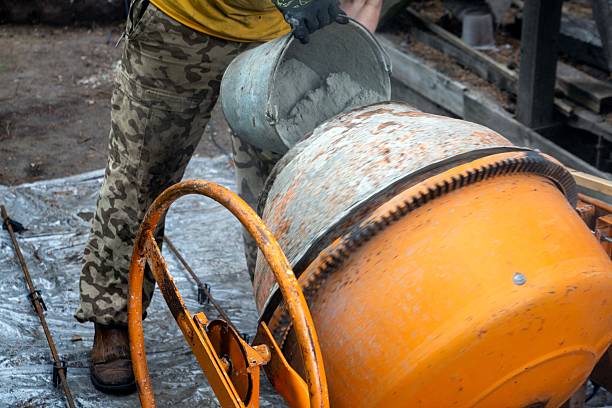 A man pours cement into a small concrete mixer
