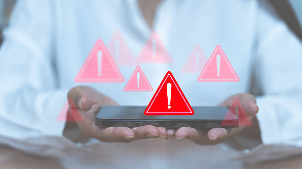 istock People holds a smartphone with red warning icons above it, symbolizing cyber threats, errors, or security alerts on mobile. 2232398118