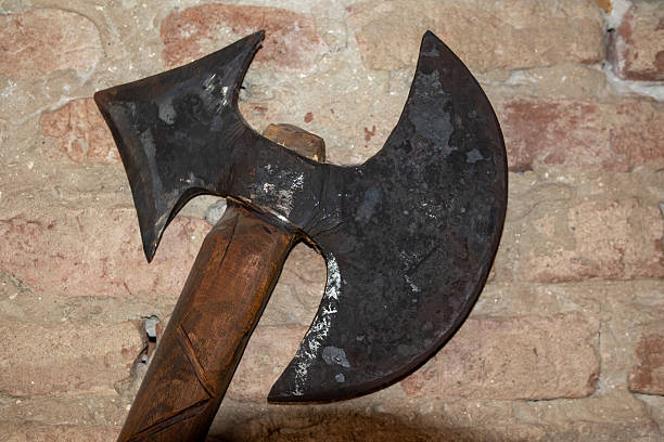 medieval battle axe with a double-edged blade and a wooden handle, hanging on a rustic brick wall.