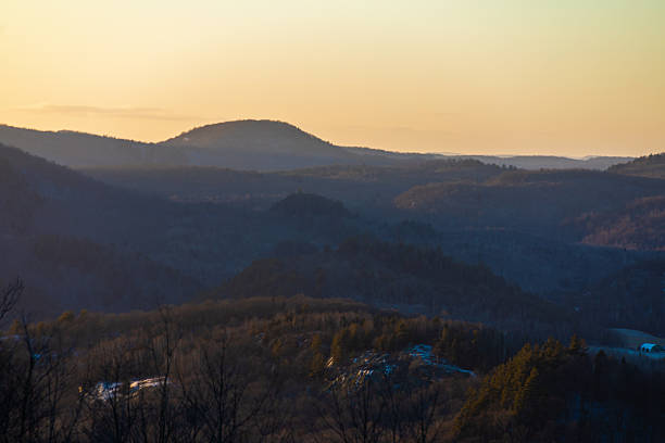 A tranquil twilight scene showing rolling hills and forested valleys illuminated by a serene sunset sky, evoking peace and natural beauty.