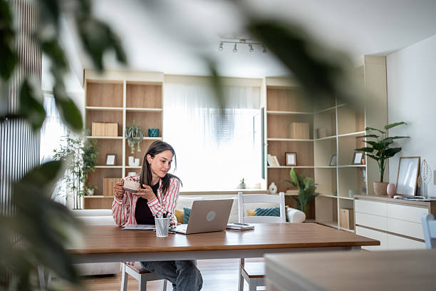 istock Young woman working from home, drinking coffee and using laptop 2232410493