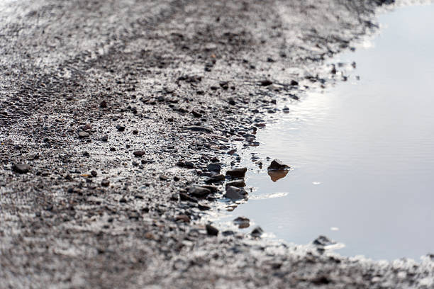 istock Rough dirt road with puddle reflecting cloudy sky after recent rain 2232413956