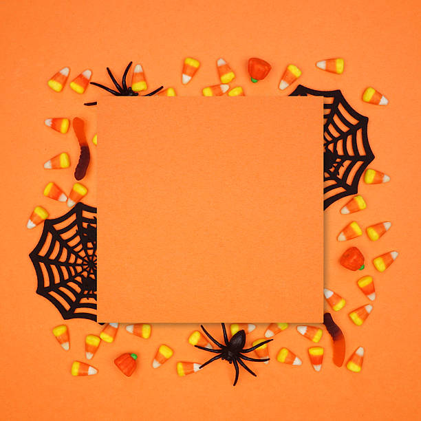 Halloween square frame of scattered candy and decor surrounding orange paper with copy space over an orange background