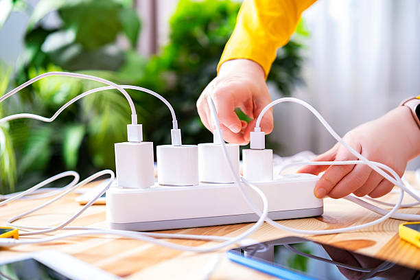istock Hand inserts gadget charger into socket with multiple devices, concept of excessive energy consumption and gadget addiction 2232417641