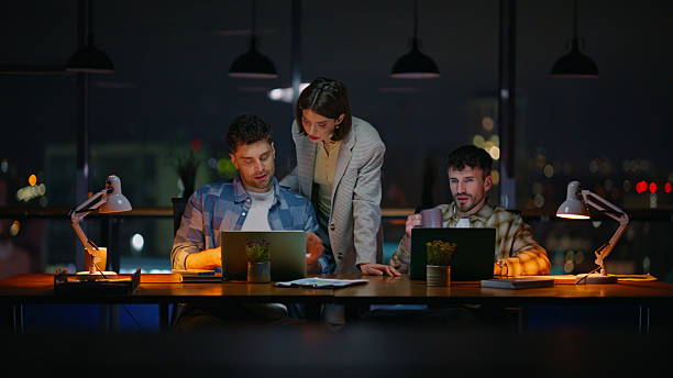 istock Lady mentor consulting managers dark windows office. Late team working laptops 2232419412