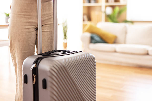 Woman holding a suitcase, preparing for a vacation in her cozy living room. Surrounded by bright, airy decor, she exudes excitement and anticipation for her upcoming journey