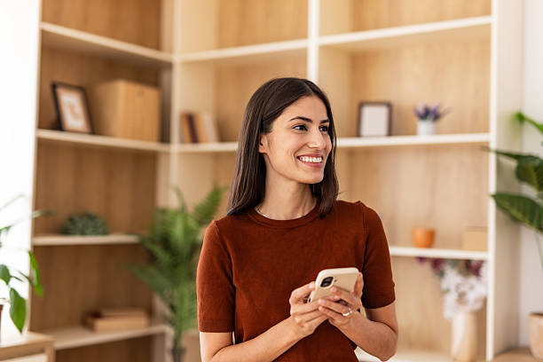 istock Young woman smiling and using mobile phone at home 2232422661