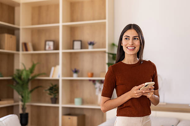 istock Young woman smiling and using smartphone at home 2232422684