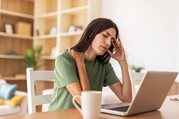 istock Young woman suffering from neck and head pain while working from home 2232423052