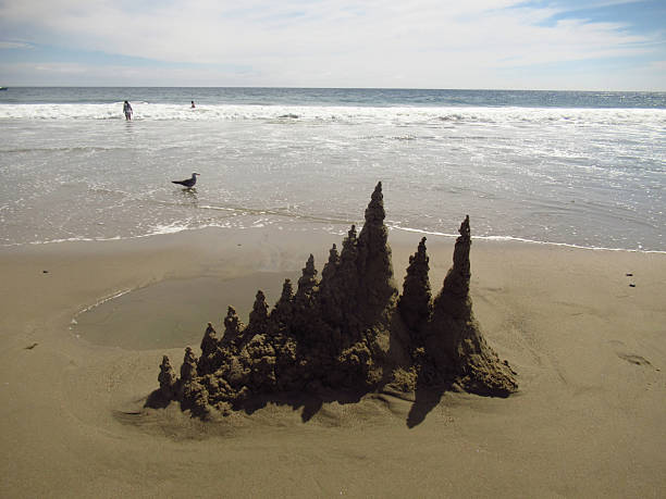 A Drip Sandcastle on the beach with a seagull and swimmers visible in the background.