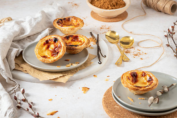 istock Several Pastel de Nata are arranged on plates with cinnamon, vanilla beans, and small golden spoons. 2232432147