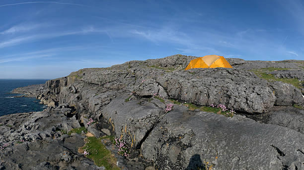An orange tent is set up near the edge of a cliff in The Burren, Ireland