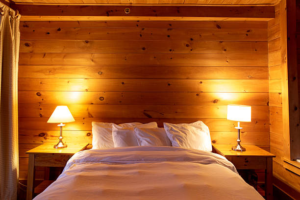 Wood-paneled bedroom featuring a neatly made bed with white linens, softly glowing bedside lamps, and a serene ambiance perfect for relaxation.