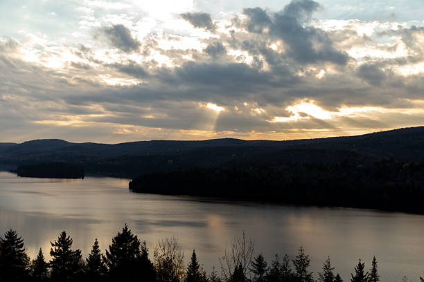 Serene landscape featuring a calm lake surrounded by wooded hills under a dramatic sunset sky.