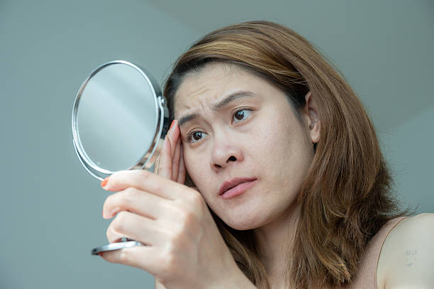 istock Asian woman using mirror to see acne and wrinkle problem on her face. 2232440363