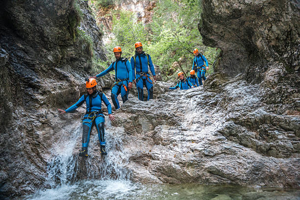 A diverse group, dressed in neoprene suits and safety helmets, slides down the canyons, making the most of their canyoning adventure.