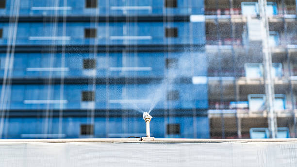 A sprinkler system is spraying water on a construction site with buildings in the background, showing industrial water management.