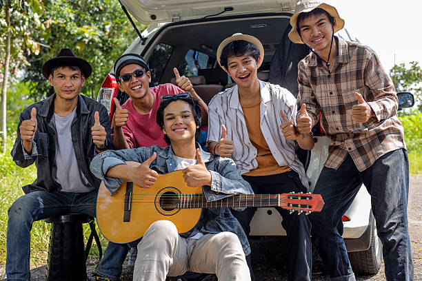 Group of Friends Sit on Car Trunk and Giving Thumbs Up, Enjoying a Trip Ride
