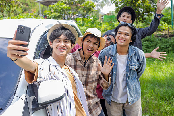 Group Of Happy Young Asian Men Taking A Selfie Outside A Car, Smiling And Waving At The Camera. Vacation With Car Concept.