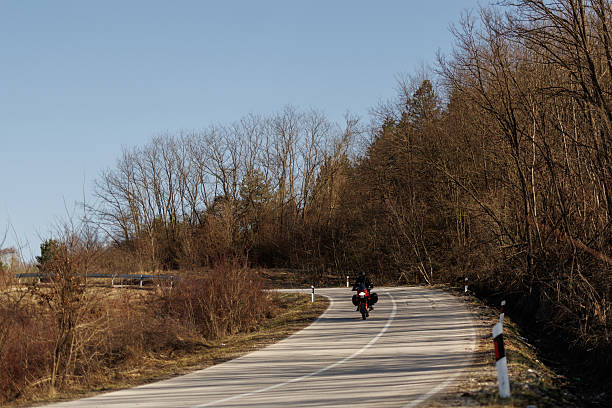 Young biker in leather suit driving his motorcycle through countryside