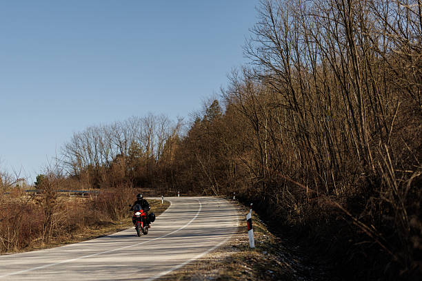 Young biker in leather suit driving his motorcycle through countryside