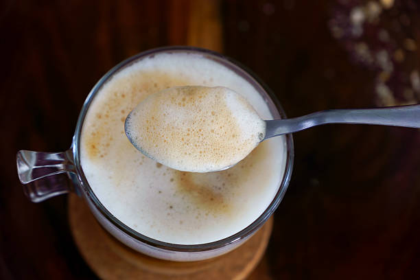 istock Spoon lifting coffee foam from glass cup on wooden table 2232453266