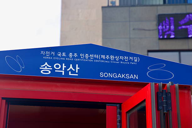 Close view of the Songaksan certification booth signage for the Jeju Circular Bicycle Path, its blue header crowning the red kiosk near the coastal trailhead.