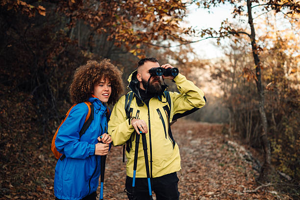 Hikers observing nature with binoculars in autumn forest
