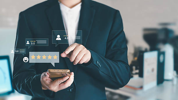 istock Businessman using a smartphone to check customer reviews. He touches a virtual screen with a five-star rating, showing satisfaction and feedback for a product or service in a modern office. 2232464883