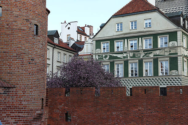 A picturesque European streetscape featuring a historic brick wall, a charming building with unique facade art, and a blossoming tree. Ideal for travel, tourism, and historical context; evokes a peaceful, nostalgic mood.  High-resolution image perfect for print and web.