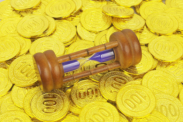 Close up of hourglass on many gold coins background.