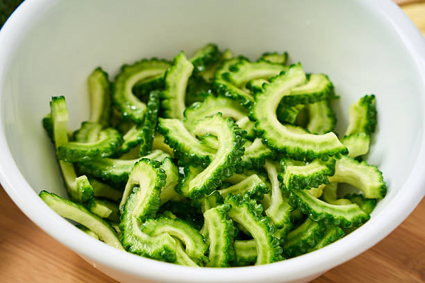 Half-moon slices of bitter melon (goya) placed in a white bowl. Bright, clean prep scene ideal for recipe steps, ingredient preparation, and summer vegetable content in Japanese or Okinawan cuisine.